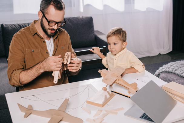happy father and son modeling wooden plane at home  - Photo, Image