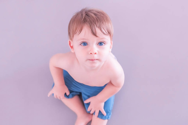Blonde baby boy with blue eyes in blue shorts sitting on a pink background - 写真・画像
