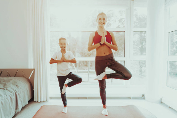 Mum And Daughter Does One Leg Standing Exercise. Active Lifestyle. Relaxing Together. Doing Fitness At Home. Holiday Leisure. Body Balance. Sport Training. Work Out On Gym Carpet. Sunny Day. - Foto, afbeelding