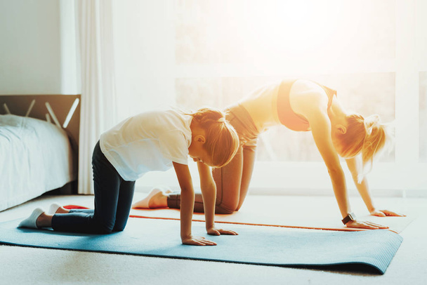 Mum And Daughter Back Stretching. Yoga Training. Active Lifestyle. Relaxing Together. Doing Fitness At Home. Holiday Leisure. Body Balance. Sport Exercise. Laying On Gym Carpet. Sunny Day. - 写真・画像