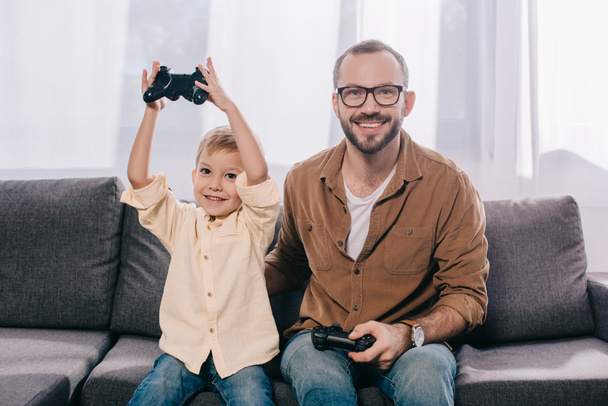 happy father and son using joysticks and smiling at camera - Φωτογραφία, εικόνα