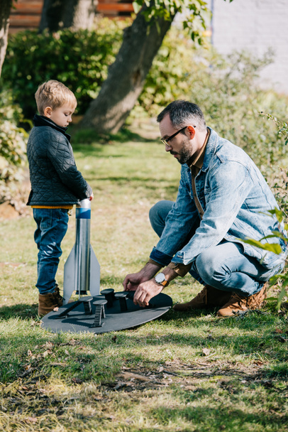 side view of father and little son launching model rocket outdoor - Fotoğraf, Görsel