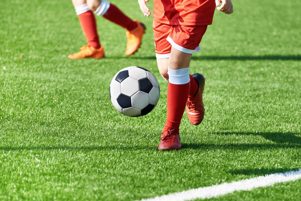 Jambes d'un joueur de football garçon en uniforme de sport rouge avec un ballon sur un terrain de football
 - Photo, image