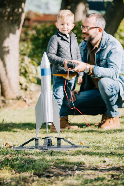 primer plano vista de modelo cohete y padre con hijo jugando detrás
 - Foto, Imagen