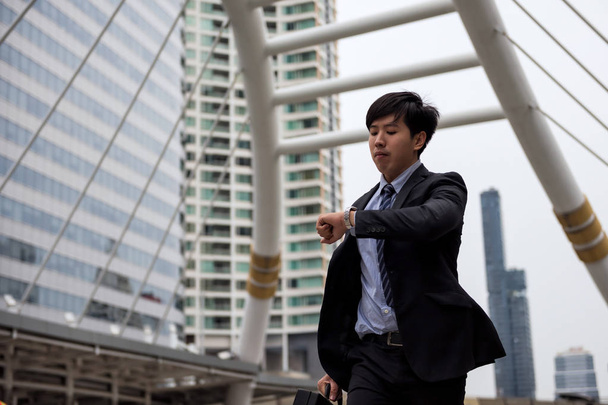 Anxious Asian businessman run and look at watch to check time on city walk in rush hour. Young man late for train transportation, work, meeting. Office life and business competition. - Photo, Image