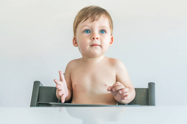 Portrait of a blonde baby boy with blue eyes sitting at the table - Fotografie, Obrázek