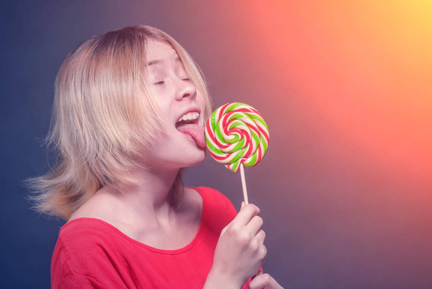 blonde girl teenager in a red blouse licks the lollipop in the sunlight - 写真・画像