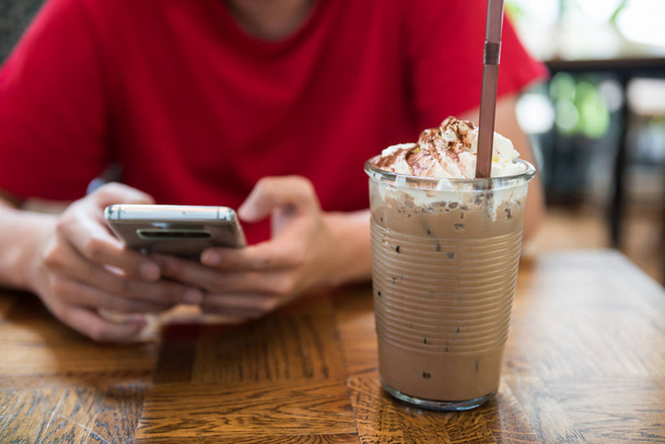 Człowiek w kawiarni przy użyciu smartfona, czatuj i social media w pobliżu Kawa mokka lodu z bicz śmietany w kawiarni. Relaks styl życia - Zdjęcie, obraz