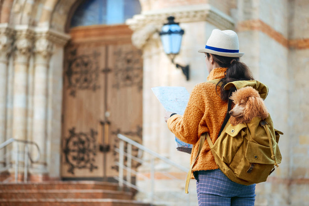 Woman traveler with dog in the backpack examines architectural monument . Concept of travel. - Photo, Image