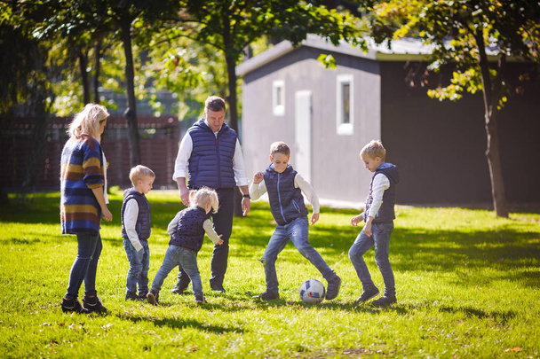 Motyw rodziny świeżym powietrzu. duże przyjazny rodzinie Kaukaska sześć mama tata i czworo dzieci gry piłki nożnej, biegania z piłką na trawniku, Zielona trawa trawnik w pobliżu domu na słoneczny dzień. - Zdjęcie, obraz
