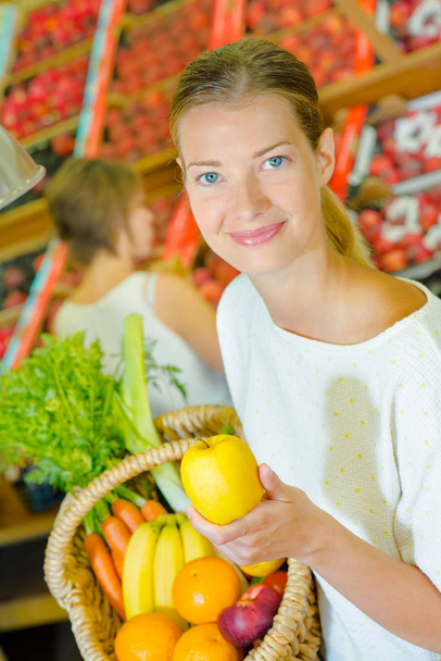 Lady holding basket of fruit and vegetables, an apple in her hand - Фото, изображение
