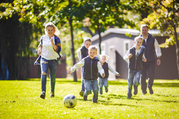 El tema de la familia actividades al aire libre. gran familia caucásica amigable de seis padres y cuatro niños jugando al fútbol, corriendo con la pelota en el césped, césped de hierba verde cerca de la casa en un día soleado
. - Foto, imagen
