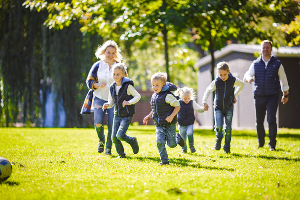 The theme family outdoor activities. big friendly Caucasian family of six mom dad and four children playing football, running with the ball on lawn, green grass lawn near the house on a sunny day. - Photo, Image