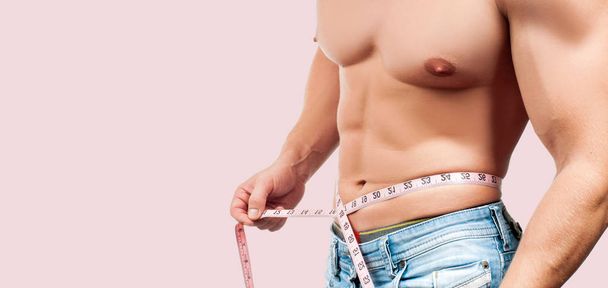 muskulöser Mann mit perfektem Körper, der seine Taille auf rosa Hintergrund misst.  - Foto, Bild