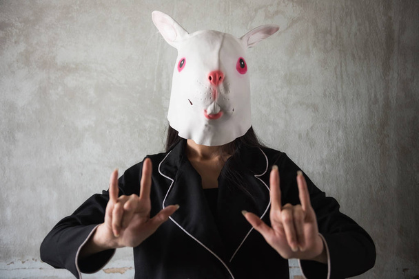 Κορίτσι με λαγουδάκι κουνέλι μάσκα δείχνει αγάπη χέρι πινακίδα με παλιά βρώμικο τοίχο υπόβαθρο και αντίγραφο χώρο για το κείμενο. Πάσχα και Απόκριες διακοπών αστεία ιδέα. Κόμμα Cosplay ζώων Latex - Φωτογραφία, εικόνα