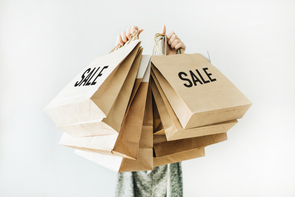 Black Friday sales discount concept. Young woman hold craft paper bags with word Sale on white background. - Fotó, kép
