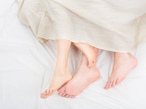Close up barefoot legs of couple lovers sleep on white bed in bedroom at morning - Photo, Image