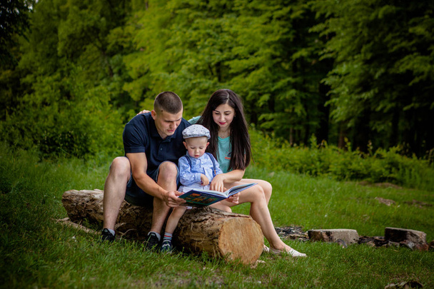 Happy mother, father and son read a book in the park - Fotó, kép