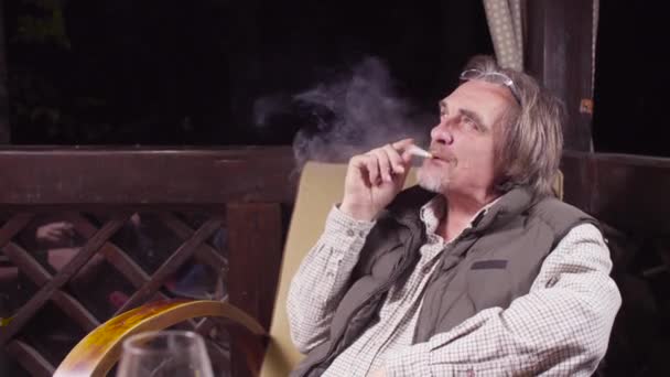 Vanhempi mies istuu tuolissa juoden viiniä ja tupakoiden
 - Materiaali, video