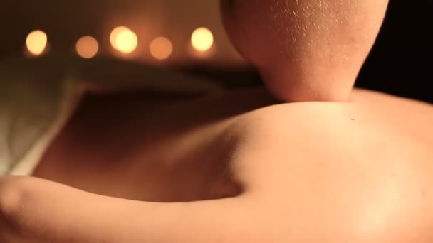 Γκρο πλαν Spa μασάζ χαμηλή γωνία. Ανδρικό μασάζ θεραπευτής κάνει μασάζ πλάτη και τους ώμους σε ένα νεαρό κορίτσι με τους αγκώνες της σε ένα σκοτεινό γραφείο ανάμεσα σε αναμμένα κεριά - Πλάνα, βίντεο