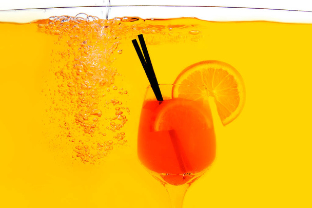 Aperol spritz cocktail in glass inside in water on a orange background. Orange juice is under the water with red and white acrylic paints. - Fotó, kép