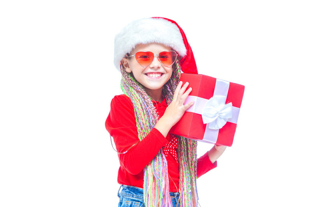 Girl in Santas hat. Portrait of little cute girl holding box of Christmas present, Small girl hug her gift with happy and fun expression isolated on white background. Holiday gift - Φωτογραφία, εικόνα