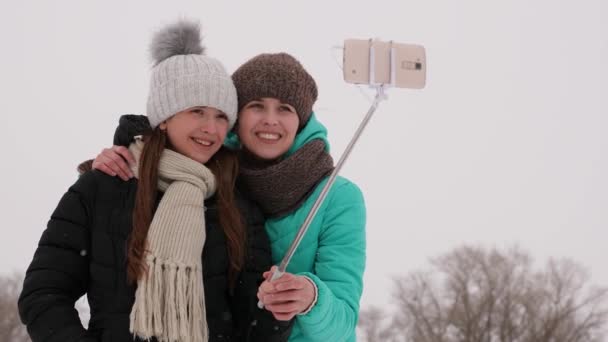 Mom and daughter are photographed on smartphone, in winter park on Christmas morning. Family resting in the snowy woods, white snow will fall. - Кадры, видео