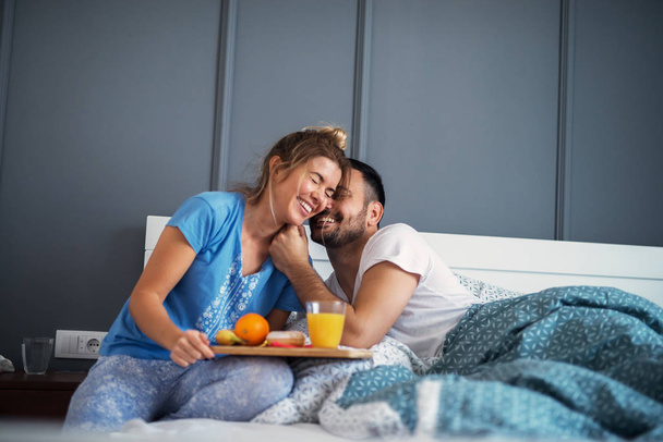 Jeune couple heureux et détendu prenant le petit déjeuner ensemble au lit. S'amuser et sourire
. - Photo, image