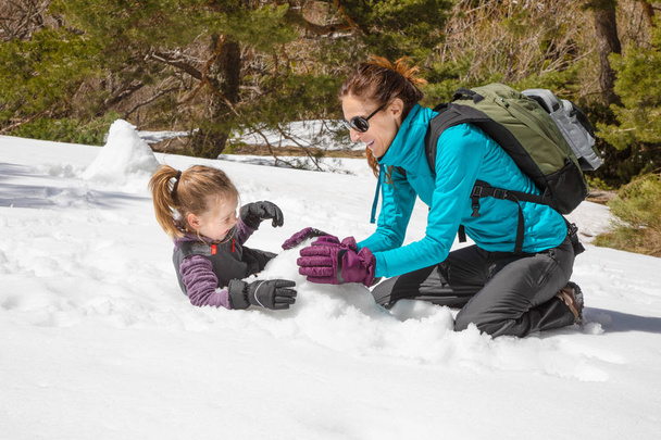 Donna felice e figlia divertente, ragazza bionda di quattro anni, seduta a ridere insieme giocando con la neve nella natura
 - Foto, immagini