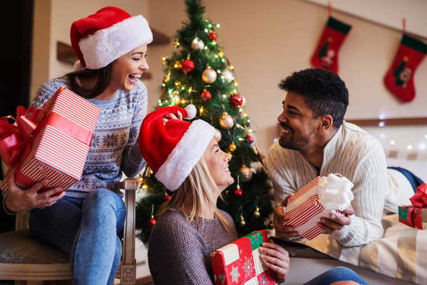 Happy přátelé nosí Santa klobouky slaví Vánoce v ložnici s mnoha dárky - Fotografie, Obrázek