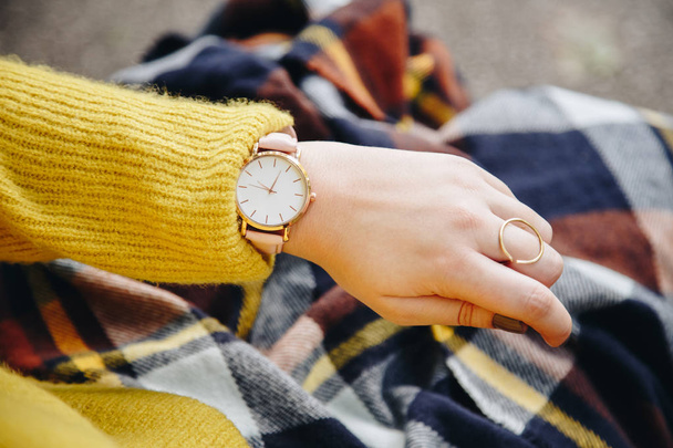 ストリート スタイル ファッションの詳細。間近で、若者のファッションのブロガーのセーターとアナログの腕時計を身に着けています。スタイリッシュな女性彼女の時計の時刻をチェックします。秋/秋のシーズン. - 写真・画像