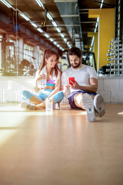 beau couple souriant assis sur le sol dans la salle de gym et de prendre selfie avec téléphone mobile
 - Photo, image