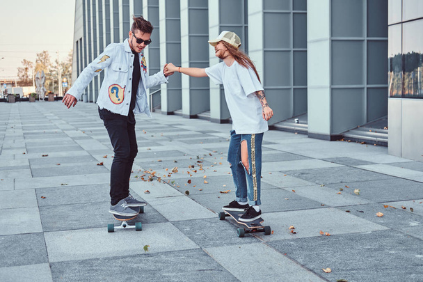 Heureux jeune couple s'amuser en conduisant des planches à roulettes sur une rue moderne
. - Photo, image