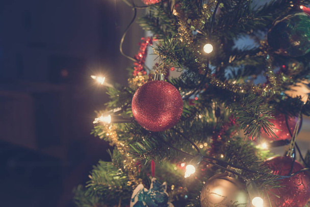 Imagen retro de adorno de Navidad rojo brillante colgando del árbol de vacaciones decorado con luces
. - Foto, imagen