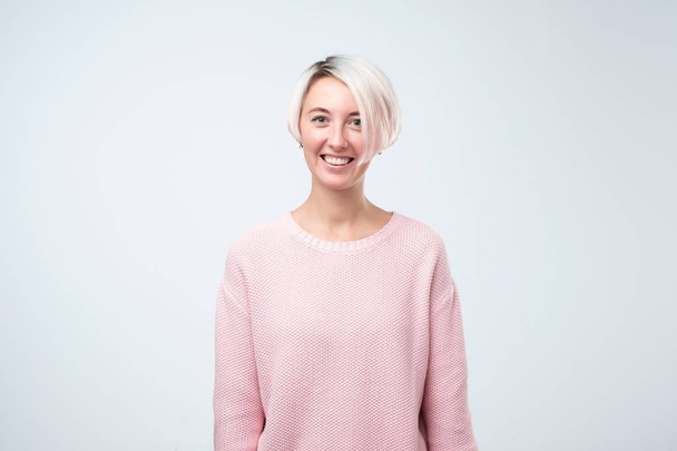 Portrét šťastná dívka s odbarvenými vlasy v růžový svetr s úsměvem při pohledu na fotoaparát. - Fotografie, Obrázek