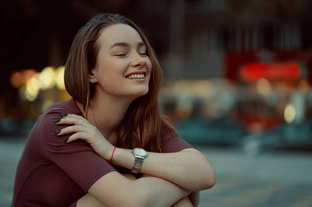 Mooi eenzaam meisje droomt en denken, toeristische jonge vrouw poseren in stad straat met gebouwen en verlichting op de achtergrond. - Foto, afbeelding