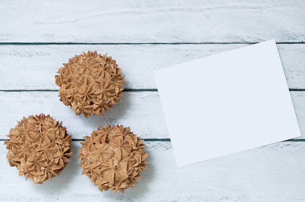 Three cupcakes with chocolate cream and a white card. White wooden background. - Zdjęcie, obraz