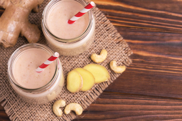 Banana and almond smoothie with ginger in glass jars with paper straws on rustic wooden table. Top view. Copy space - Foto, Imagem