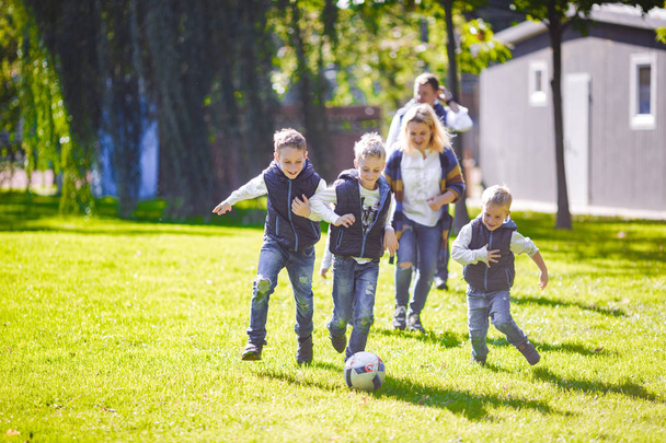 Teema perheen ulkoilu. Iso ystävällinen valkoihoinen perhe kuusi äiti isä ja neljä lasta pelaa jalkapalloa, käynnissä pallo nurmikolla, vihreä ruoho nurmikko lähellä taloa aurinkoisena päivänä
. - Valokuva, kuva