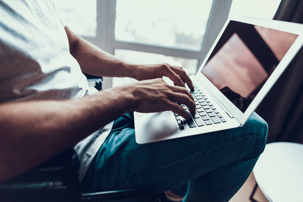 Closeup of Male Hands Typing Keyboard on Laptop. Unrecognizable Person Wears T-Shirt and Blue Jeans Sits in Wheelchair Networking Holding Notebook on Lap. Disability and Work Concept - Фото, зображення