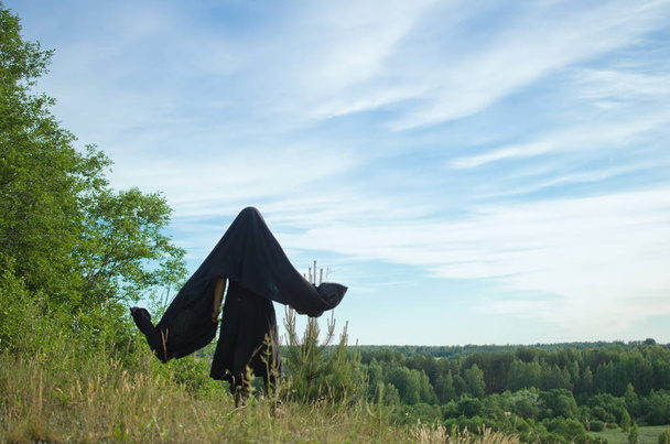 donna strega in un mantello nero guarda nel bosco da una montagna coperta di erba
 - Foto, immagini