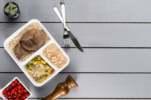 Белая фасоль коричневый рис с колбасой и овощами. Бразильская коробка для обеда. Впереди приготовление пищи или диета концепции. вид сверху
. - Фото, изображение