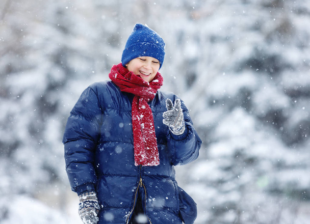 милый мальчик в синей куртке играет в снежки в зимнем парке. Зимние мероприятия
.  - Фото, изображение