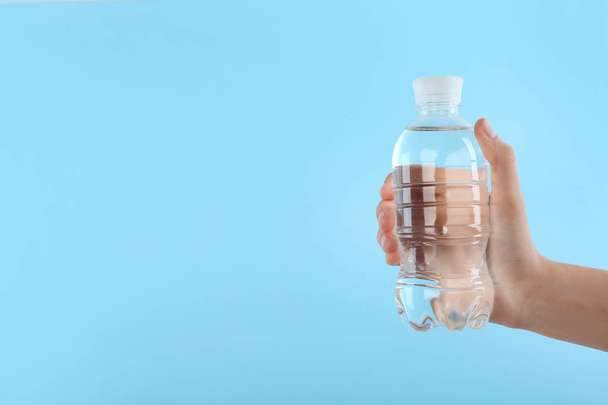 Woman holding plastic bottle with water on color background. Space for text - Foto, Bild