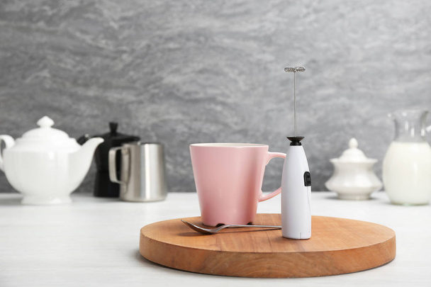 Board with milk frother and cup of coffee on table. Space for text - Foto, afbeelding