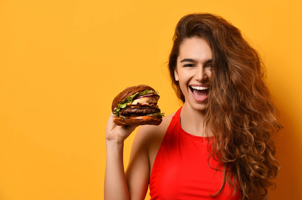 Woman hold big barbecue burger sandwich with hungry mouth happy screaming laughing on yellow background - Фото, зображення