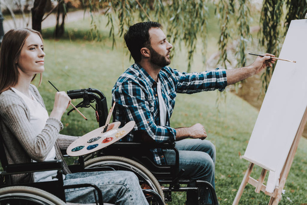 Disabled Young Man on Wheelchairs Drawing in Park. Disabled Young Man. Smiling Woman. Relaxing in Summer Park. Fun in Summer Park. Recovery and Healthcare Concepts. Cheerful People. - Foto, Imagen