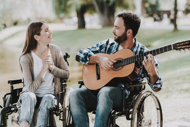Disabled Man on Wheelchairs Playing Guitar in Park. Disabled Young Man. Woman on Wheelchair. Relaxing in Summer Park. Fun in Summer Park. Recovery and Healthcare Concepts. Cheerful People. - Fotografie, Obrázek