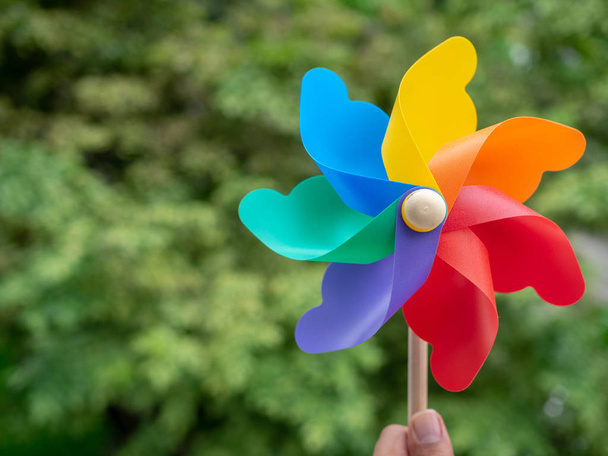 Χέρι που κρατά το πολύχρωμο pinwheel σε φόντο πράσινο της φύσης με αντίγραφο χώρου. - Φωτογραφία, εικόνα