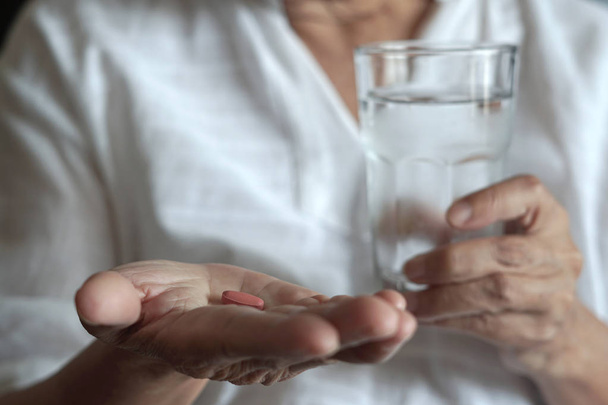 mulher idosa está comendo remédio e com pílulas e copo de água em casa
 - Foto, Imagem